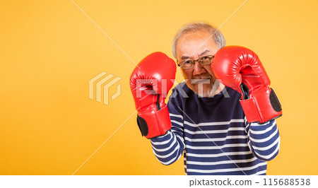 Portrait Asian old man wearing glasses wear two red boxing gloves studio shot isolated yellow background, smiling happy elderly man gray haired healthy fighter lifestyle concept 115688538