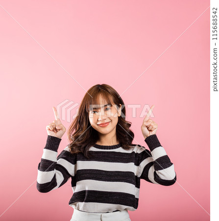 Asian happy portrait beautiful cute young woman standing makes gesture two fingers point upwards above presenting product something, studio shot isolated on pink background with copy space Asian happy portrait beautiful cute young woman standing makes gesture two fingers point upwards above presenting product something, studio shot isolated on pink background with copy space 115688542