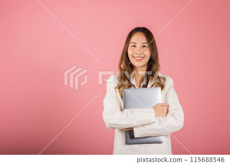 Front view woman smiling confident smiling holding closed laptop, Portrait excited happy Asian young female person hugging close cover computer device studio shot isolated on pink background 115688546