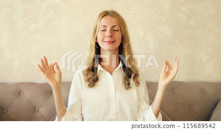 Calm relaxed healthy young woman meditates, practicing yoga sitting on the couch at home Calm relaxed healthy young woman meditates, practicing yoga sitting on the couch at home 115689542