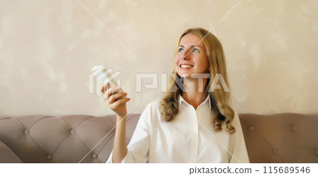 Happy smiling caucasian young woman turns on the air conditioner using the remote control at home 115689546