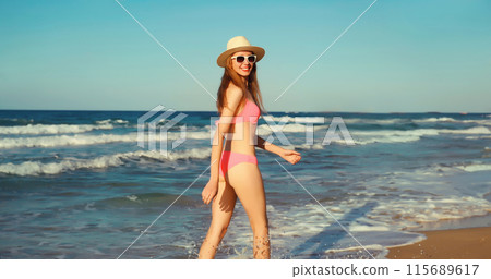 Summer vacation, happy young woman walking running in bikini, tourist hat on the beach on sea coast 115689617