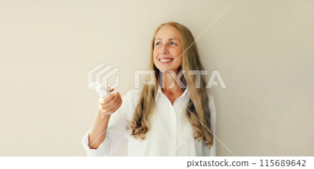 Happy smiling middle-aged woman turns on the air conditioner or TV using the remote control 115689642