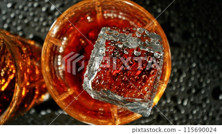 Closeup of ice cube falling into glass of whiskey. 115690024