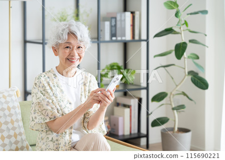 Senior woman using a smartphone in the living room 115690221