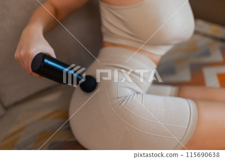 Gun shock vibration percussion massage therapy. Sporty woman practicing self-massaging your legs close up. Applying therapeutic percussive massage gun in living room at home indoors. Copy text space Gun shock vibration percussion massage therapy. Sporty woman practicing self-massaging your legs close up. Applying therapeutic percussive massage gun in living room at home indoors. Copy text space 115690638