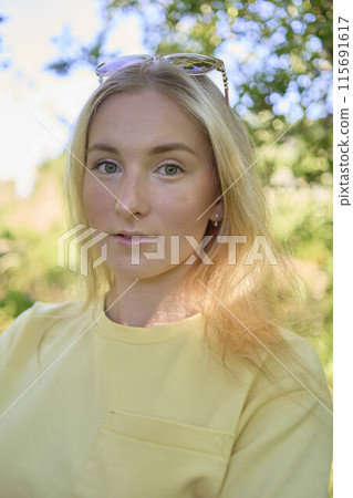 a portrait of a young blond girl in a yellow T-shirt and shorts among the trees on a summer day a portrait of a young blond girl in a yellow T-shirt and shorts among the trees on a summer day 115691617