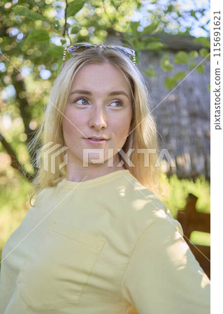 a portrait of a young blond girl in a yellow T-shirt and shorts among the trees on a summer day 115691621