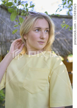 a portrait of a young blond girl in a yellow T-shirt and shorts among the trees on a summer day a portrait of a young blond girl in a yellow T-shirt and shorts among the trees on a summer day 115691623