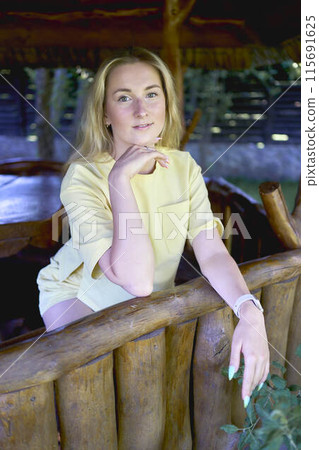 portrait of a young blonde girl in a yellow T-shirt and shorts in a wooden gazebo portrait of a young blonde girl in a yellow T-shirt and shorts in a wooden gazebo 115691625
