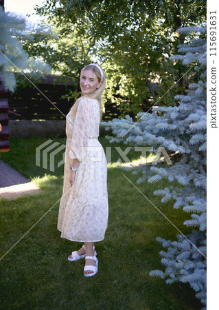 portrait of a young blonde girl in a pastel chiffon dress near a blue Christmas tree 115691631