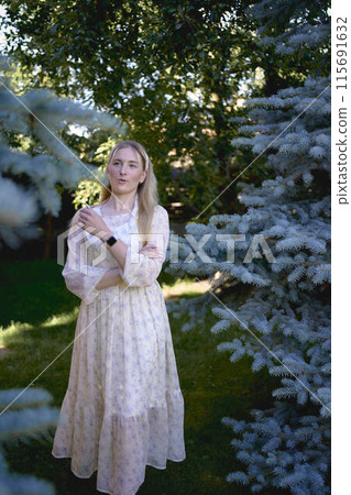 portrait of a young blonde girl in a pastel chiffon dress near a blue Christmas tree 115691632