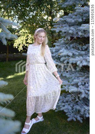 portrait of a young blonde girl in a pastel chiffon dress near a blue Christmas tree 115691636