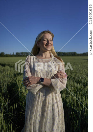 portrait of a young blonde woman in a pastel chiffon dress in a green wheat field 115691656