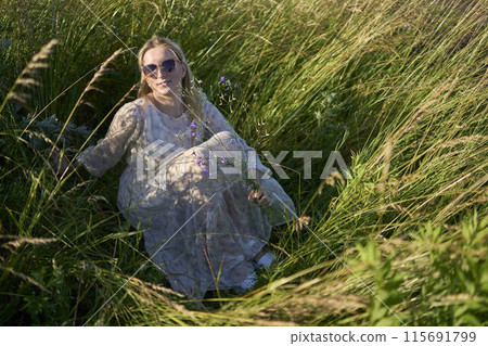 portrait of a young blonde woman in a pastel chiffon dress in a field of golden grass 115691799