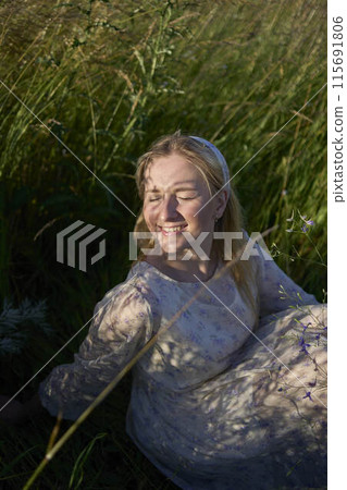 portrait of a young blonde woman in a pastel chiffon dress in a field of golden grass 115691806