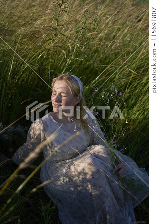 portrait of a young blonde woman in a pastel chiffon dress in a field of golden grass portrait of a young blonde woman in a pastel chiffon dress in a field of golden grass 115691807