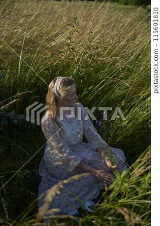 portrait of a young blonde woman in a pastel chiffon dress in a field of golden grass portrait of a young blonde woman in a pastel chiffon dress in a field of golden grass 115691810