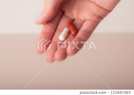 Female hand holding the capsules on pink background. Fingers holding pills, closeup. Concept of health care, dietary supplements, vitamins, treatment of depression and diseases. High quality photo Female hand holding the capsules on pink background. Fingers holding pills, closeup. Concept of health care, dietary supplements, vitamins, treatment of depression and diseases. High quality photo 115691965