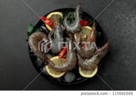 Large King prawns on lemon slices and ice. Hot peppers. Black plate. Black background 115692089