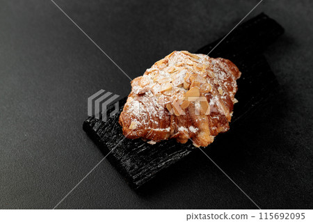 Almond croissant. puff pastry, delicate frangipane cream with almonds, enriched with butter. On top, the croissant has a hint of almond flakes and powdered sugar. on a black cutting board 115692095