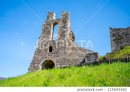 The ancient ruins of Potstejn Castle stand against a bright blue sky, surrounded by lush green grass. The old stone walls are a popular historical site in Czechia. The ancient ruins of Potstejn Castle stand against a bright blue sky, surrounded by lush green grass. The old stone walls are a popular historical site in Czechia. 115693482