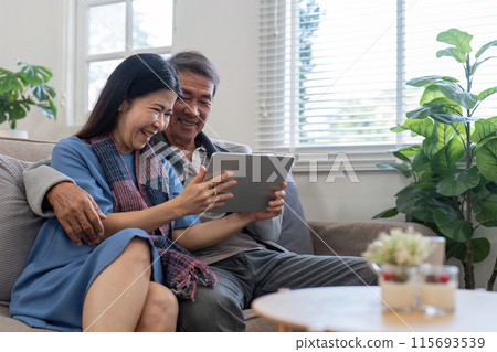 Elderly Couple Enjoying Quality Time Together at Home with Tablet in Cozy Living Room Elderly Couple Enjoying Quality Time Together at Home with Tablet in Cozy Living Room 115693539