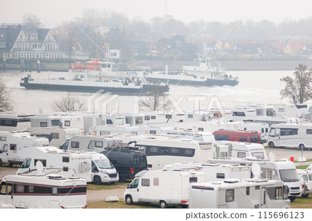 RV camper van parking place at Warnemunde Rostock harbor canal cruise liner pier ferry vessel ship background. Many recreational vehicle parked Germany port harbor foggy day. Travel tourism adventure 115696123