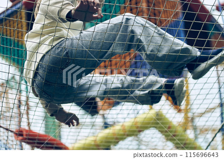 A small child is having fun in a rope park, jumping on a grid. Classes at a summer camp for children. An adventure park with a copy space. High quality photo 115696643