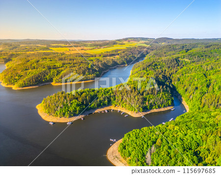 Orlik Water Reservoir in Czechia. Scenic aerial view of the Vltava River with lush forests, a peninsula, and peaceful waters with boats docked. Orlik Water Reservoir in Czechia. Scenic aerial view of the Vltava River with lush forests, a peninsula, and peaceful waters with boats docked. 115697685