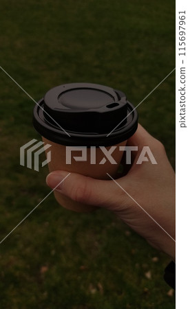 Hand holding cup of coffee, under green grass, mobile photo, vertical 115697961