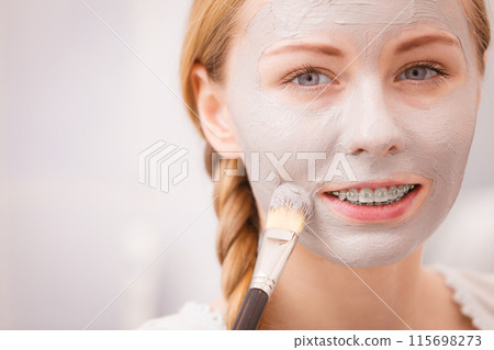 Happy young woman applying mud mask on face 115698273