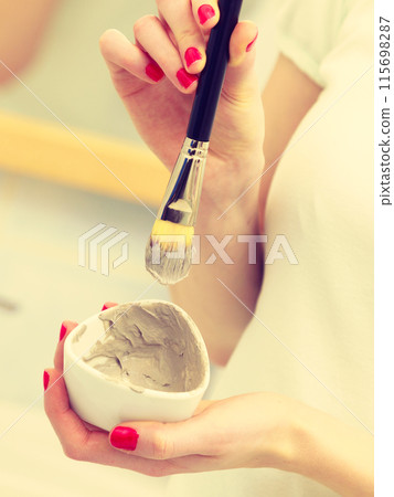 Female hand holding clay mud mask and brush. Skin care. 115698287