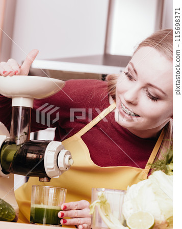 Woman in kitchen making vegetable smoothie juice 115698371