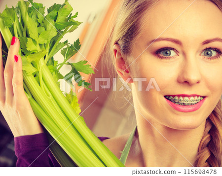 Woman in kitchen holds green celery 115698478