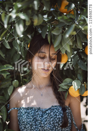 Woman in a sunlit orchard, surrounded by orange trees, portraying tranquility and natures beauty Woman in a sunlit orchard, surrounded by orange trees, portraying tranquility and natures beauty 115698778