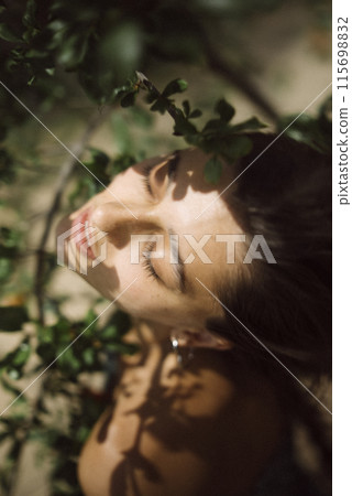 A woman peacefully enjoying the sunlight surrounded by natures greenery and foliage 115698832