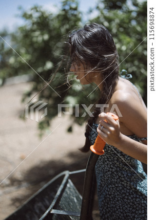 A youthful lady is having fun outdoors while playing with an orange water gun in the sunshine A youthful lady is having fun outdoors while playing with an orange water gun in the sunshine 115698874