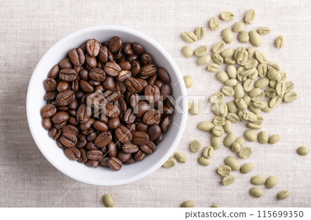 Roasted coffee beans in a white bowl on linen fabric. On the right unroasted green Arabica coffee beans, seeds of berries from Coffea arabica, also Arabian, mountain or arabica coffee. Close-up. Photo 115699350