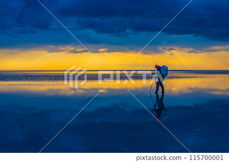 Photographer capturing breathtaking sunset over reflective water scene 115700001