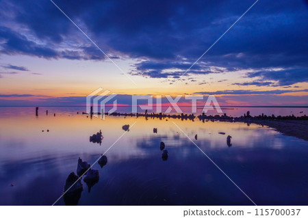 Serene sunset over calm water with dark sky and wooden posts Serene sunset over calm water with dark sky and wooden posts 115700037