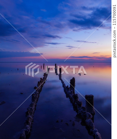 Serene sunset over calm waters with wooden structures 115700091