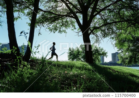 Man running in a park with skyscrapers in the background 115700400