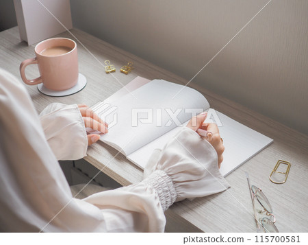 A woman drinking coffee and opening a notebook 115700581