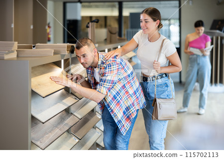 Interested couple selecting laminate floorboards in building hypermarket Interested couple selecting laminate floorboards in building hypermarket 115702113
