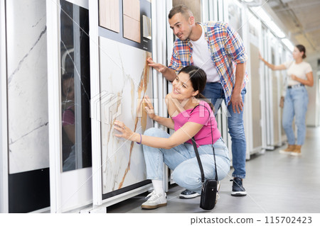 Couple examining tile samples displayed on sliding stand in store 115702423