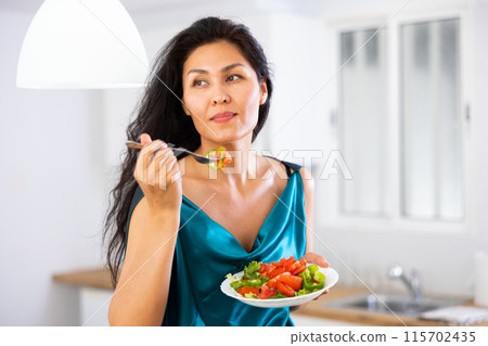Portrait of woman in nightdress eating salad at home 115702435