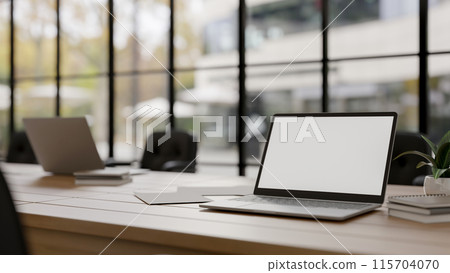 A laptop computer with a white screen mockup on a meeting table in a modern meeting room. 115704070
