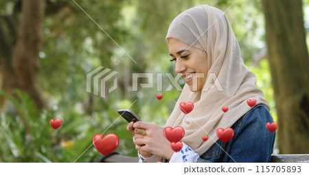 Muslim woman in hijab texts with hearts flying around her on a bench in 4k. 115705893
