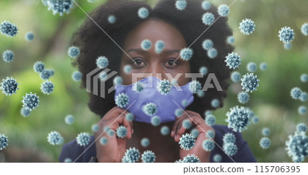 Image of coronavirus cells over african american woman putting on face mask in park 115706395
